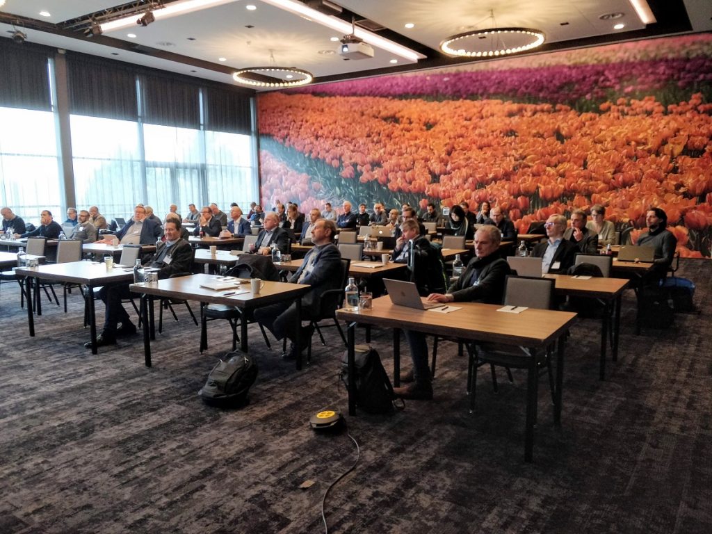 People sitting at individual tables in a conference room, each is in front of a laptop.